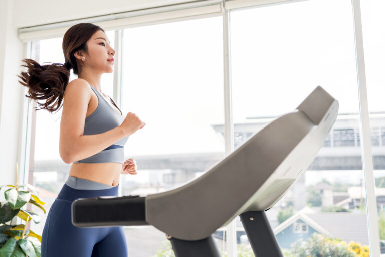 A woman jogging on a treadmill in a bright, modern gym, highlighting fitness and wellness in an indoor setting. Indoor working out at home concept.