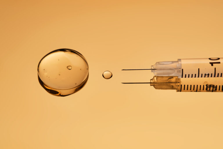 A syringe with a drop of a medical drug on a golden background.