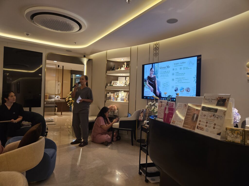 ทีมงานถือไมโครโฟนแนะนำตนเองหน้าจอ About Me และผู้ร่วมประชุมนั่งรับฟัง